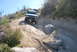 1996 Ford Bronco - Two SUVs navigate a challenging off-road trail with large rocks and sparse vegetation.