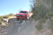 1996 Ford Bronco - Off-road Bronco navigating a rocky trail with brush and trees in the background.