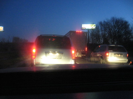 Silver minivans and a truck in traffic at dusk, with brake lights illuminated