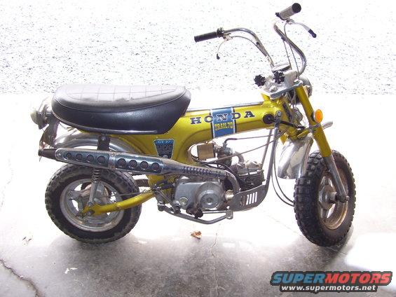 Yellow 1970 Honda CT70 Trail motorcycle, side view, showing black seat, chrome exhaust, and 'Honda Trail 70' decal