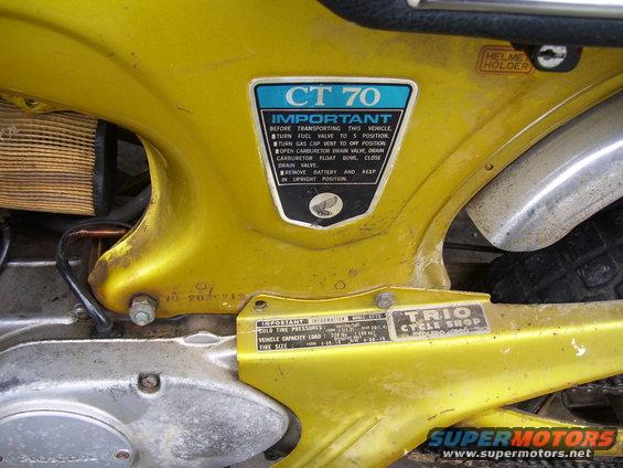 Close-up of yellow Honda CT70 frame with "CT 70" sticker and "Trio Cycle Shop" decal