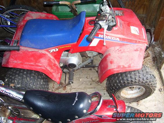 Red ATV with blue seat and '70 Fourtrax' decal, parked next to a bicycle and another vehicle