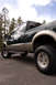 2003 Ford F-350 - This dark green and tan pickup truck is shown from a 3/4 front angle, highlighting its build and off-road tires.