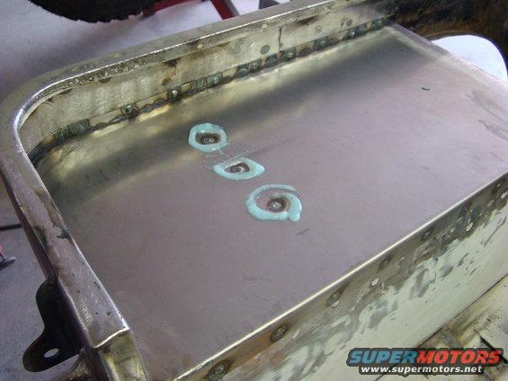 Metal panel with three circular blue sealant applications and visible weld spots