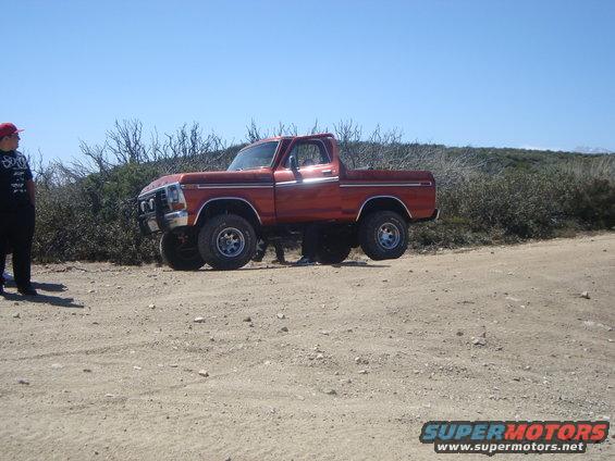 Orange 1979 Ford F-150 4x4 pickup truck with lifted suspension on a dirt road
