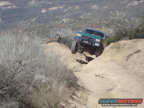 Green SUV going down a steep, rocky trail. Looks like a 1987 Ford Bronco