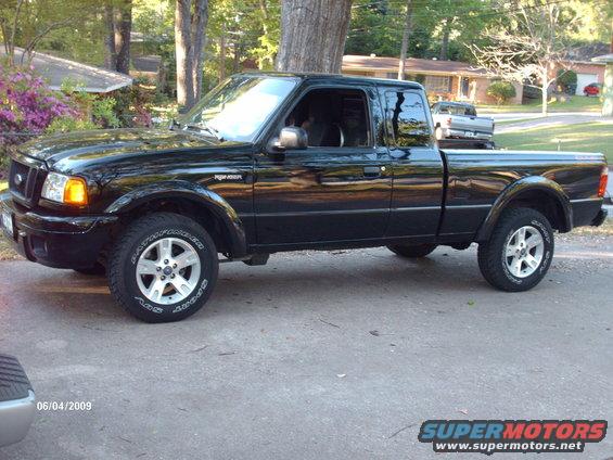 Black Ford Ranger pickup truck parked on a driveway. Another truck is visible in the background