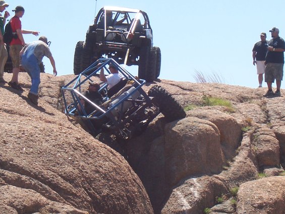 Two off-road vehicles are navigating a rocky incline, one is tilted precariously