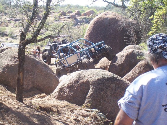 Blue off-road buggy with number 57 on its side climbs over large rocks