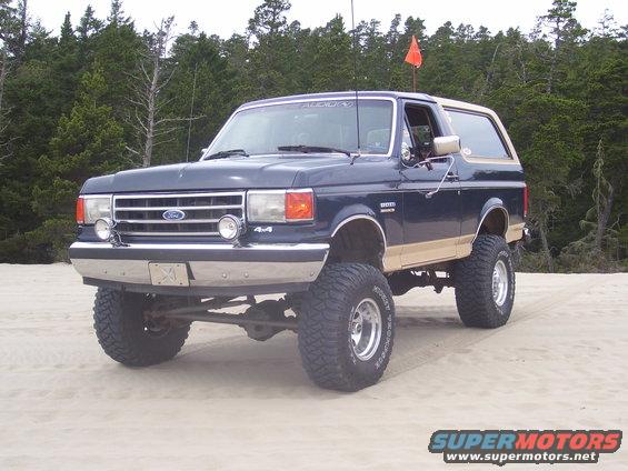 Dark blue 1991 Ford Bronco with tan trim, lifted on large tires, parked on sand dunes