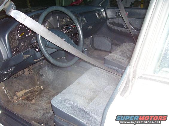 Car interior showing dashboard, steering wheel, driver's seat, and passenger seat. Seatbelt is across the seats