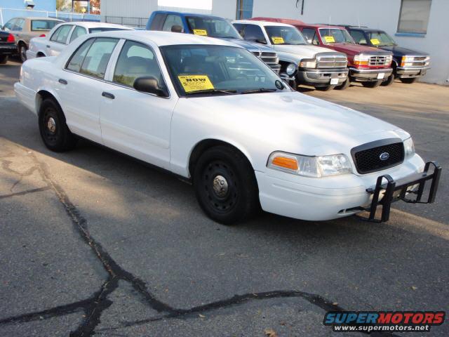 White 2004 Ford Crown Victoria with push bumper parked on asphalt, other vehicles in background