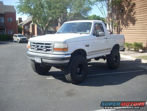 1992 Ford Bronco lifted with large tires parked in a lot, another SUV in background