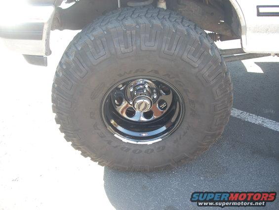 Close-up of a large off-road tire on a black rim with chrome lug nuts