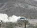 1984 Dodge Power Ram - Off-road truck driving through dust on a desert track, with another vehicle partially visible.