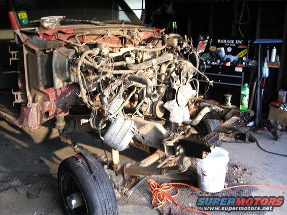 Truck chassis with engine removed, sitting in a garage with tools and a bucket nearby