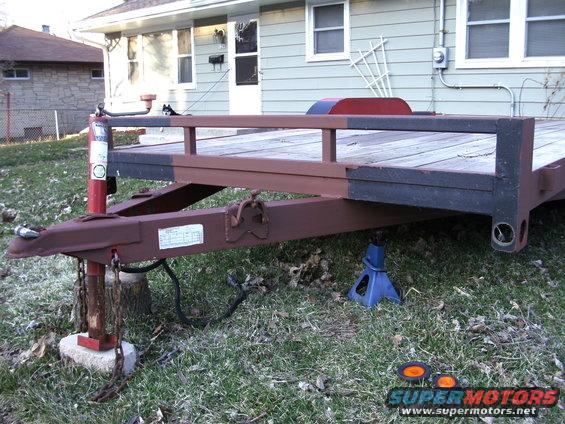 Trailer hitch assembly with chains and a wooden deck, supported by a jack stand