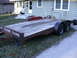2005 Ford F-250 - A utility trailer with a wooden deck is parked on grass in front of a residential building.