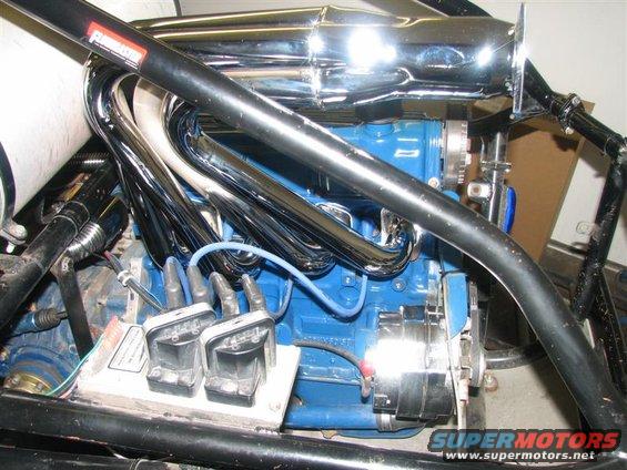 Close-up of a blue engine with chrome headers, spark plug wires, and an alternator