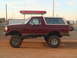 1992 Ford Bronco - A lifted maroon 1992 Ford Bronco with a tan removable top is seen from the side in a dirt lot.