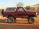 1992 Ford Bronco - This lifted 1992 Ford Bronco is parked on a dirt lot with a house in the background.