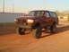 1992 Ford Bronco - A lifted red 1992 Ford Bronco is parked on a dirt road under a clear sky.