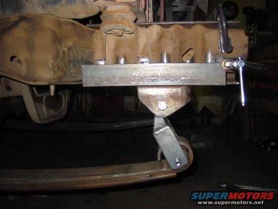 Custom metal bracket attached to vehicle frame, holding a roller against a leaf spring