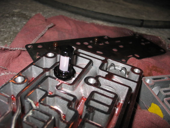 Transmission valve body disassembled, showing internal passages and a filter. Red fluid is visible
