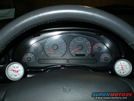 Car dashboard with speedometer, tachometer, fuel gauge, and two aftermarket gauges (boost and fuel pressure)