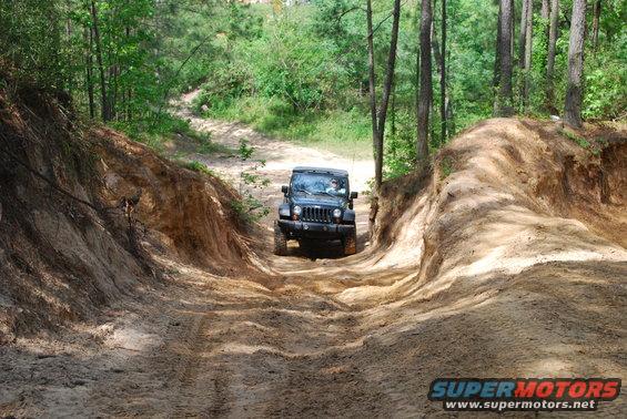 Black Jeep Wrangler driving on a dirt path through woods