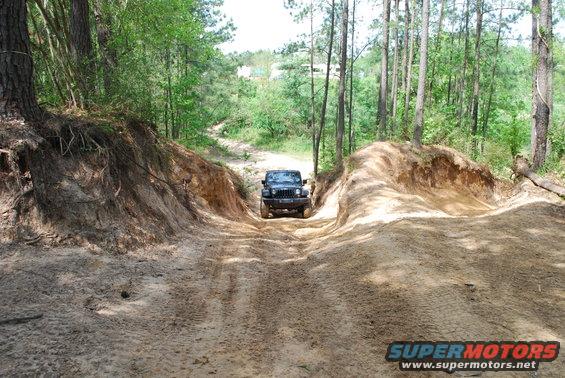 2008 Jeep Wrangler driving up a sandy hill on a wooded trail