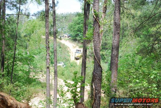 Three off-road vehicles on a dirt path through a wooded area