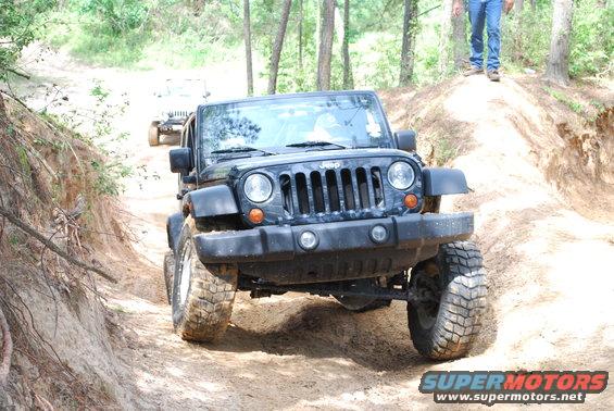 Black Jeep Wrangler with large tires driving on a dirt trail, front view