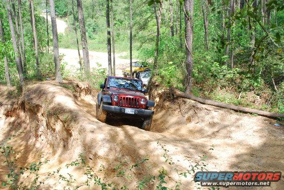 Red Jeep Wrangler driving on a dirt trail with other vehicles behind it