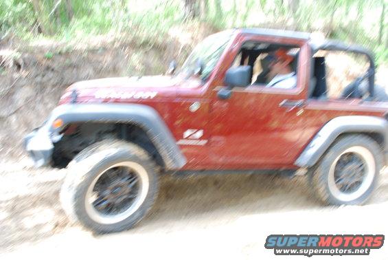Red 2008 Jeep Wrangler driving on a dirt path with trees in background