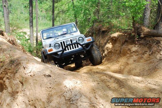 White Jeep Wrangler with aftermarket bumper on a steep dirt incline