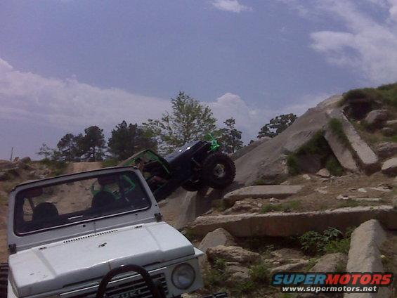 White off-road vehicle front view, with another vehicle climbing rocks in background