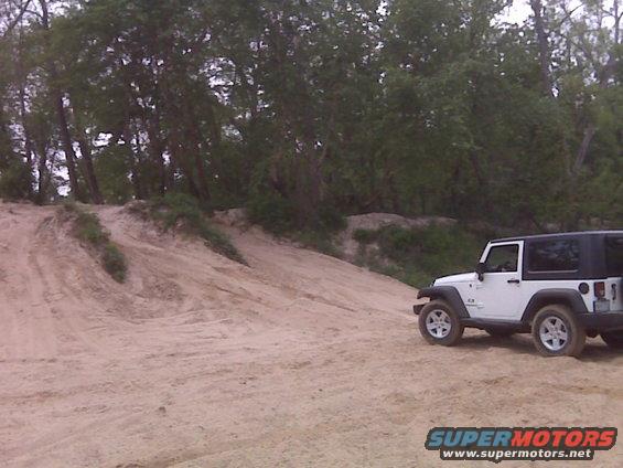 White 2007 Jeep Wrangler parked on a sandy hill with trees in the background