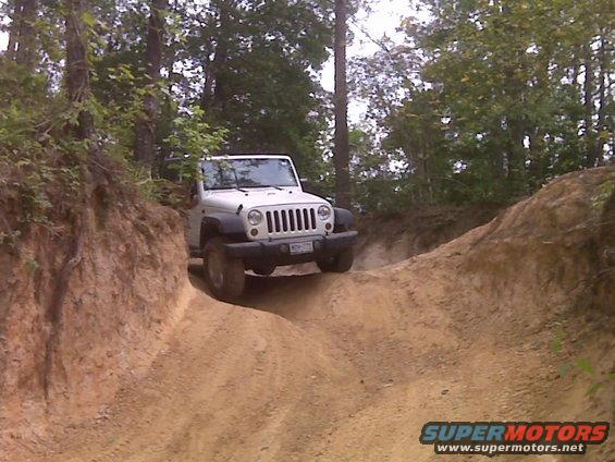 White Jeep Wrangler driving on a steep dirt trail with trees on either side