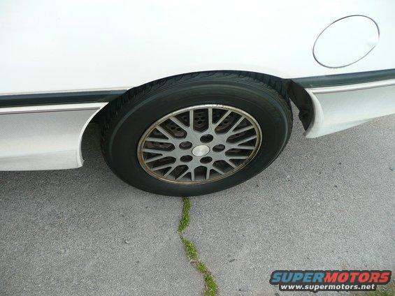 White car's rear wheel and fender with a gas cap door visible