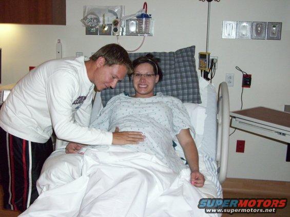 Couple in hospital room, woman in bed with man placing hand on her pregnant belly