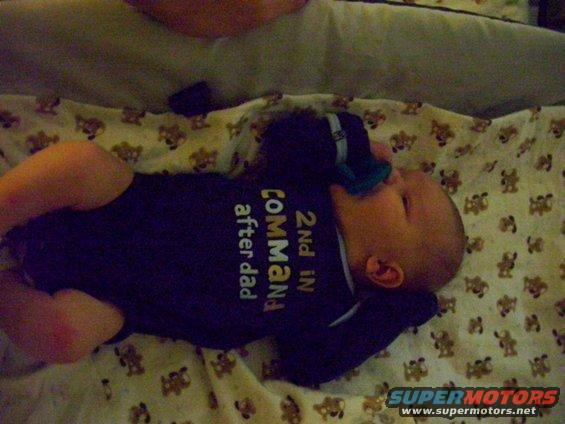 Baby in a crib wearing a dark blue onesie that says '2nd in command after dad'