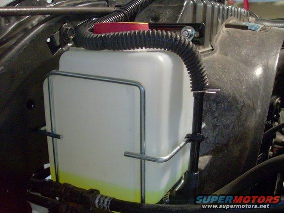 Windshield washer fluid reservoir with yellow fluid, black hose, and metal bracket