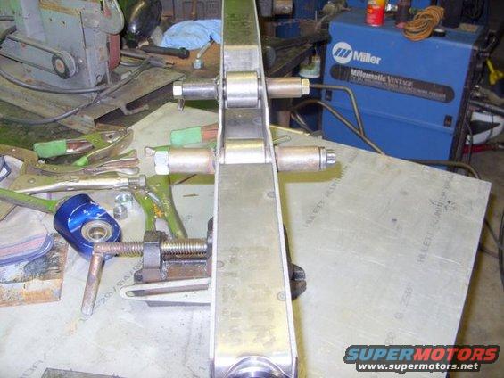 Close-up of a metal suspension component with visible bolts and rollers, clamped in a vise