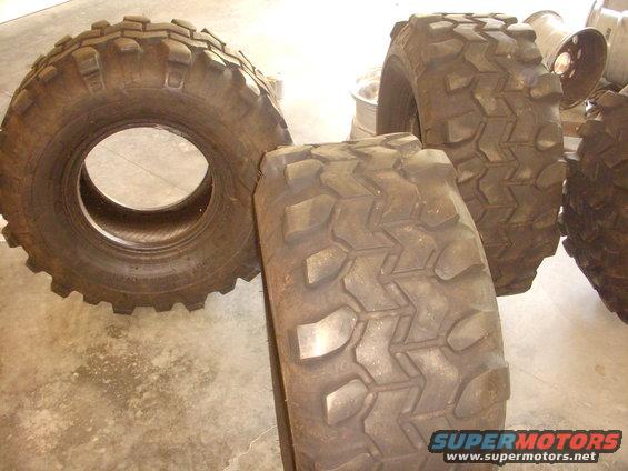 Several large off-road tires with aggressive tread patterns on a concrete floor.