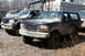1995 Ford Bronco - Several muddy trucks are parked in a lot with some industrial equipment in the background.