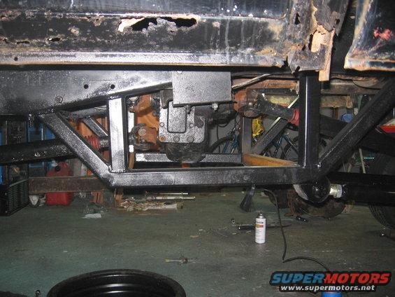 Underside of a vehicle showing the transmission, frame, and suspension components. Some rust is visible on the body