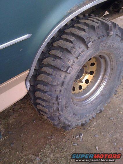 Close-up of a large off-road tire and part of a dark green vehicle's fender flare