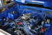 1989 Ford Mustang - Engine bay of a 1989 Ford Mustang features a V8 engine with a prominent carburetor and vibrant blue paint.