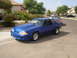 1989 Ford Mustang - A blue 1989 Ford Mustang is parked on a street with houses in the background.